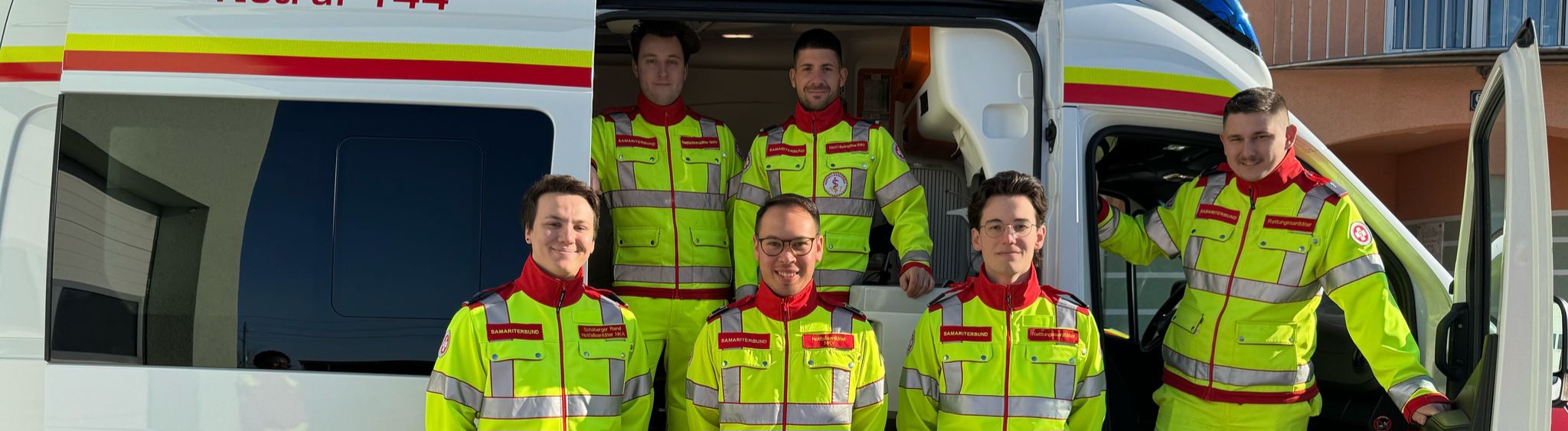 Sechs Sanitäter stehen vor einem Rettungsauto.